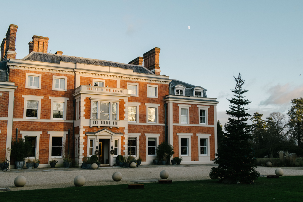 Exterior of large country house hotel Heckfield Place with frost on the lawn and christmas tree