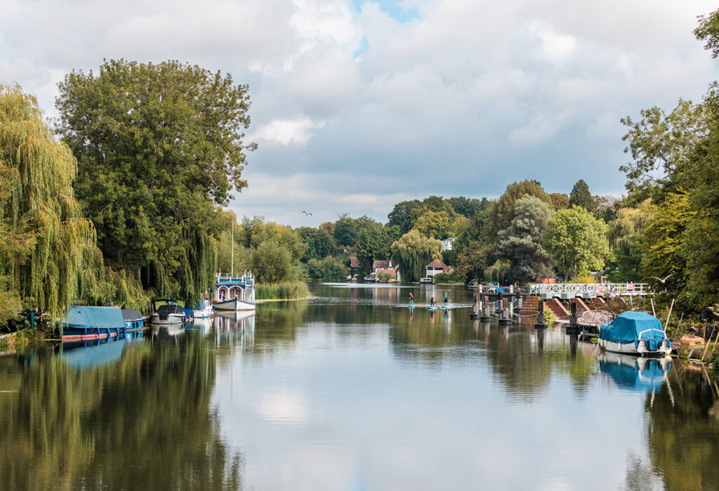 River view of Goring and Streatley, England, with boats and paddle boarders and trees lining the river